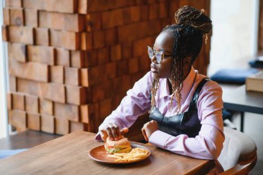 Afro saçlı Afrikalı bir kadın leziz bir klasik burgerle patates kızartması yiyor. Hile Yemeği.