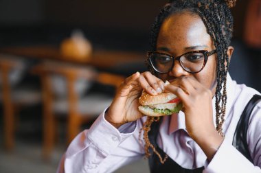 Afro saçlı Afrikalı bir kadın leziz bir klasik burgerle patates kızartması yiyor. Hile Yemeği.