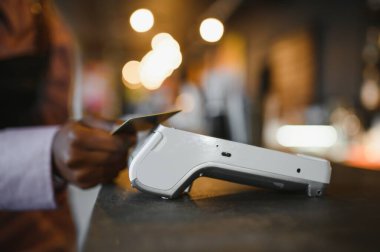 NFC teknolojisinin yanında kredi kartı tutan kadın müşteri, terminal üzerinden ödeme faturası yapıyor.