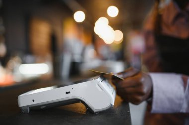 NFC teknolojisinin yanında kredi kartı tutan kadın müşteri, terminal üzerinden ödeme faturası yapıyor.