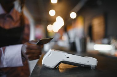 NFC teknolojisinin yanında kredi kartı tutan kadın müşteri, terminal üzerinden ödeme faturası yapıyor.