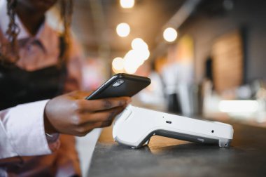 NFC teknolojisinin yanında kredi kartı tutan kadın müşteri, terminal üzerinden ödeme faturası yapıyor.