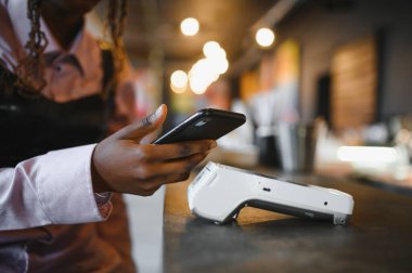 NFC teknolojisinin yanında kredi kartı tutan kadın müşteri, terminal üzerinden ödeme faturası yapıyor.