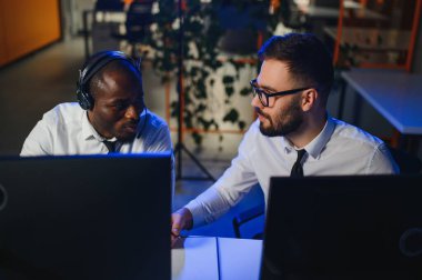 Mutlu Güvenilir Teknik Müşteri Destek Uzmanı Meslektaşlar ve Ekranlarla Dolu Gözetleme ve Kontrol Odasında Kulaklık Çağrısı Yapıyor.