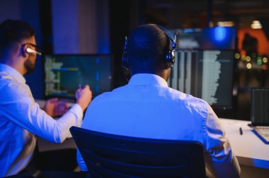 Mutlu Güvenilir Teknik Müşteri Destek Uzmanı Meslektaşlar ve Ekranlarla Dolu Gözetleme ve Kontrol Odasında Kulaklık Çağrısı Yapıyor.