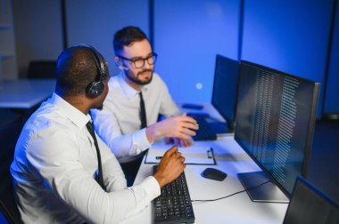 Mutlu Güvenilir Teknik Müşteri Destek Uzmanı Meslektaşlar ve Ekranlarla Dolu Gözetleme ve Kontrol Odasında Kulaklık Çağrısı Yapıyor.