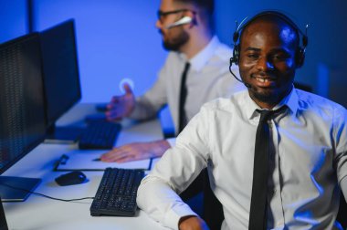 Mutlu Güvenilir Teknik Müşteri Destek Uzmanı Meslektaşlar ve Ekranlarla Dolu Gözetleme ve Kontrol Odasında Kulaklık Çağrısı Yapıyor.