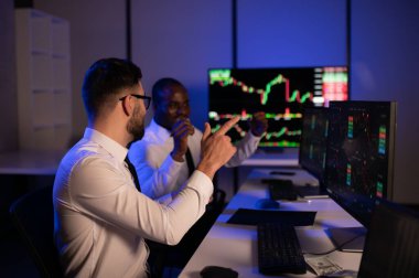 İki işadamı, finans analisti ya da yatırım danışmanı ellerinde polis bilgisayarları ve belgelerle büro masasında oturuyorlar.