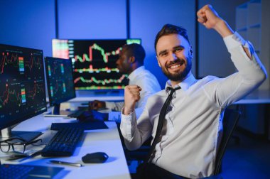 İki işadamı, finans analisti ya da yatırım danışmanı ellerinde polis bilgisayarları ve belgelerle büro masasında oturuyorlar.