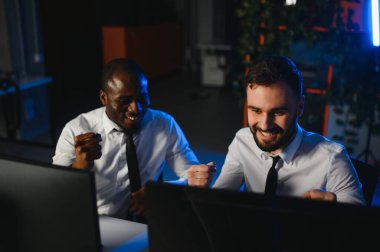 İki işadamı, finans analisti ya da yatırım danışmanı ellerinde polis bilgisayarları ve belgelerle büro masasında oturuyorlar.