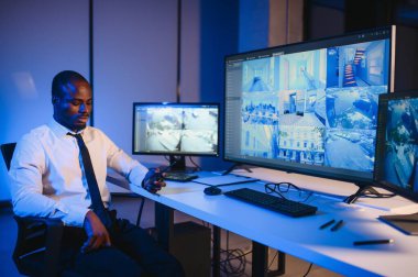 Telsizle konuşurken masaüstü bilgisayar ekranına bakan Afrikalı Amerikalı güvenlik görevlisi.