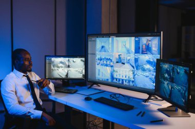 Telsizle konuşurken masaüstü bilgisayar ekranına bakan Afrikalı Amerikalı güvenlik görevlisi.