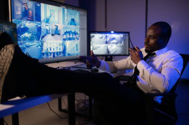 Telsizle konuşurken masaüstü bilgisayar ekranına bakan Afrikalı Amerikalı güvenlik görevlisi.