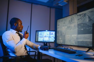 Afro-Amerikan güvenlik görevlisi ya da merkez bilgisayar ve telsiz kullanıyor, ekranlara bakıyor..