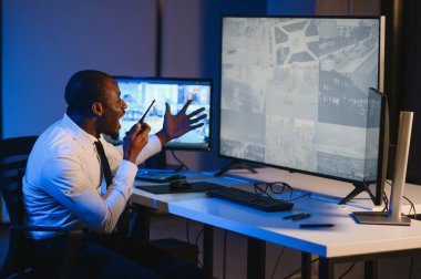 Afro-Amerikan güvenlik görevlisi ya da merkez bilgisayar ve telsiz kullanıyor, ekranlara bakıyor..