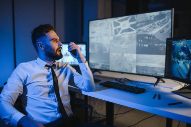 Erkek güvenlik görevlisi, bilgisayardaki birden fazla CCTV görüntüsünü izlerken telsizden konuşuyor..