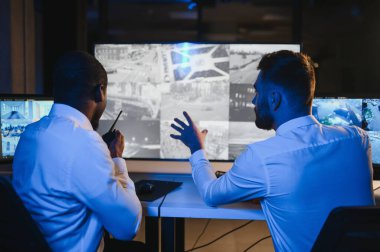 Güvenlik Kontrol Odası İki Subay Şüpheli Faaliyetler İçin Çoklu Ekranları İzlerken Telsiz ile İzinsiz Faaliyetler Raporluyorlar. Ulusal Önemliliğin İtirazını Korurlar.