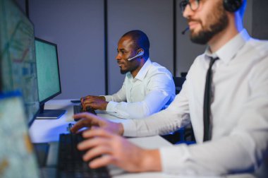 Mutlu Güvenilir Teknik Müşteri Destek Uzmanı Meslektaşlar ve Ekranlarla Dolu Gözetleme ve Kontrol Odasında Kulaklık Çağrısı Yapıyor.