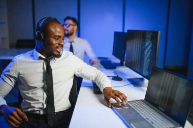 Mutlu Güvenilir Teknik Müşteri Destek Uzmanı Meslektaşlar ve Ekranlarla Dolu Gözetleme ve Kontrol Odasında Kulaklık Çağrısı Yapıyor.