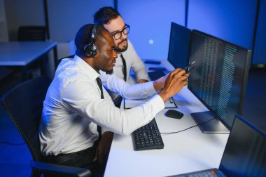 Erkek Veri Bilimadamı, Büyük Altyapı Kontrol ve İzleme Odası 'nda Kulaklık Takan Kişisel Bilgisayarda Çalışıyor. İş Çağrı Merkezi Ofisi 'nde Genç Mühendis