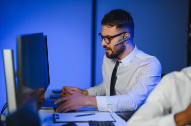 Mutlu Güvenilir Teknik Müşteri Destek Uzmanı Meslektaşlar ve Ekranlarla Dolu Gözetleme ve Kontrol Odasında Kulaklık Çağrısı Yapıyor.