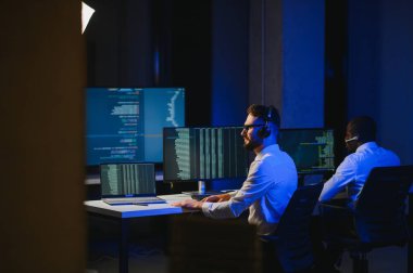 Erkek Veri Bilimadamı, Büyük Altyapı Kontrol ve İzleme Odası 'nda Kulaklık Takan Kişisel Bilgisayarda Çalışıyor. İş Çağrı Merkezi Ofisi 'nde Genç Mühendis