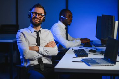 Mutlu Güvenilir Teknik Müşteri Destek Uzmanı Meslektaşlar ve Ekranlarla Dolu Gözetleme ve Kontrol Odasında Kulaklık Çağrısı Yapıyor.