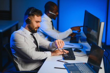 Erkek Veri Bilimadamı, Büyük Altyapı Kontrol ve İzleme Odası 'nda Kulaklık Takan Kişisel Bilgisayarda Çalışıyor. İş Çağrı Merkezi Ofisi 'nde Genç Mühendis
