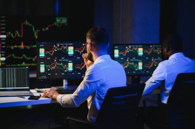 Finansal Analizci İş Gecesinde Yatırım Bankeriyle Konuşuyor. Çoklu Monitör Çalışma İstasyonunda Gerçek Zaman Stok Çizelgesi Verisi Hakkında Sohbet