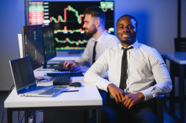 Afro-amerikan borsa bürosunda çalışan borsacı veya komisyoncu. Arka planda veri, saat numaraları ve grafikleri gösteren monitörlerin bilgisayarını kullanıyor..