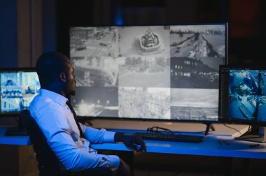 Afro-Amerikan güvenlik operatörünün arka görüntüsü. Güvenlik kamerası görüntülerini gösteren ekranları olan bir bilgisayar kullanın. .