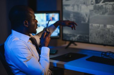 Afro-Amerikan güvenlik operatörünün arka görüntüsü. Güvenlik kamerası görüntülerini gösteren ekranları olan bir bilgisayar kullanın. .