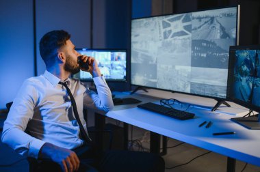 CCTV görüntülerine bakarken telsiz kullanan güvenlik sistemi operatörünün yan görüntüsü.