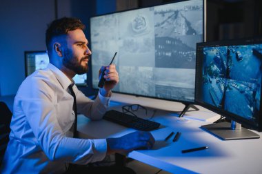 CCTV görüntülerine bakarken telsiz kullanan güvenlik sistemi operatörünün yan görüntüsü.