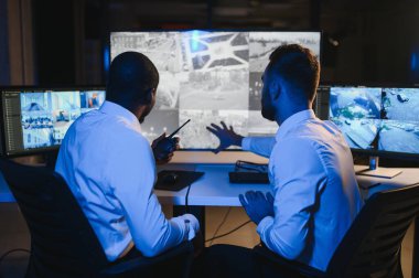 Güvenlik Kontrol Odası İki Subay Şüpheli Faaliyetler İçin Çoklu Ekranları İzlerken Telsiz ile İzinsiz Faaliyetler Raporluyorlar. Ulusal Önemliliğin İtirazını Korurlar.