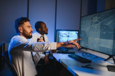 İki erkek güvenlik görevlisi bilgisayar ekranına bakarken biri videonun detaylarını anlatıyor..