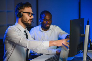 Erkek Veri Bilimadamı, Büyük Altyapı Kontrol ve İzleme Odası 'nda Kulaklık Takan Kişisel Bilgisayarda Çalışıyor. İş Çağrı Merkezi Ofisi 'nde Genç Mühendis