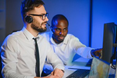 Mutlu Güvenilir Teknik Müşteri Destek Uzmanı Meslektaşlar ve Ekranlarla Dolu Gözetleme ve Kontrol Odasında Kulaklık Çağrısı Yapıyor.