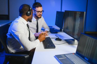 Erkek Veri Bilimadamı, Büyük Altyapı Kontrol ve İzleme Odası 'nda Kulaklık Takan Kişisel Bilgisayarda Çalışıyor. İş Çağrı Merkezi Ofisi 'nde Genç Mühendis