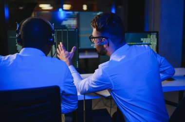 Mutlu Güvenilir Teknik Müşteri Destek Uzmanı Meslektaşlar ve Ekranlarla Dolu Gözetleme ve Kontrol Odasında Kulaklık Çağrısı Yapıyor.