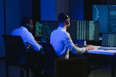 Erkek Veri Bilimadamı, Büyük Altyapı Kontrol ve İzleme Odası 'nda Kulaklık Takan Kişisel Bilgisayarda Çalışıyor. İş Çağrı Merkezi Ofisi 'nde Genç Mühendis