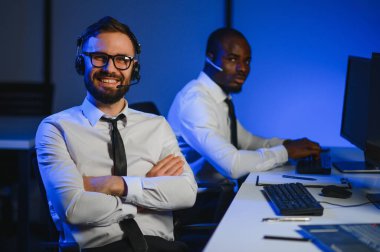 Çağrı merkezinde eller ücretsiz kulaklık kullanırken müşteriye bir şey açıklamaya çalışan erkek teknik destek ajanı.