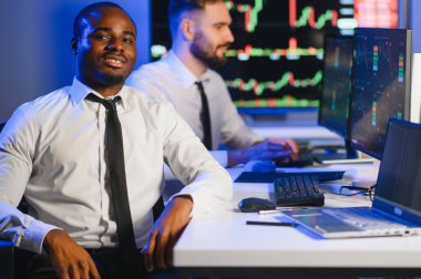 Afro-amerikan borsa bürosunda çalışan borsacı veya komisyoncu. Arka planda veri, saat numaraları ve grafikleri gösteren monitörlerin bilgisayarını kullanıyor..