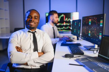 Afro-amerikan borsa bürosunda çalışan borsacı veya komisyoncu. Arka planda veri, saat numaraları ve grafikleri gösteren monitörlerin bilgisayarını kullanıyor..
