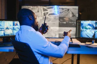 Afro-Amerikan güvenlik operatörünün arka görüntüsü. Güvenlik kamerası görüntülerini gösteren ekranları olan bir bilgisayar kullanın. .