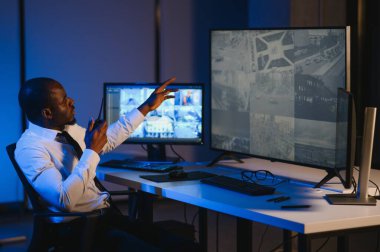 Ciddi bir Afrikalı Amerikalı güvenlik görevlisi güvenlik odasında güvenlik kamerası görüntülerini izlerken bilgisayar ekranından otel hayatını izliyor.