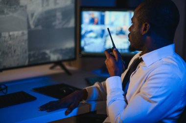 Afro-Amerikan güvenlik görevlisi ya da merkez bilgisayar ve telsiz kullanıyor, ekranlara bakıyor..