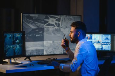 CCTV görüntülerine bakarken telsiz kullanan güvenlik sistemi operatörünün yan görüntüsü.