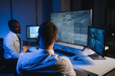 İki erkek güvenlik görevlisi bilgisayar ekranına bakarken biri videonun detaylarını anlatıyor..