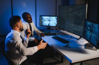 İki erkek güvenlik görevlisi bilgisayar ekranına bakarken biri videonun detaylarını anlatıyor..